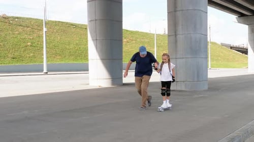 Father Teaching Daughter How to Skateboard Outdoors