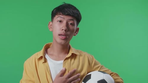 Close Up Of Asian Boy With A Ball Singing National Anthem While Cheering Soccer On Green Screen
