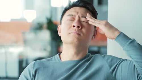 Young exhausted, overworked office worker sitting on a couch with a severe headache massaging