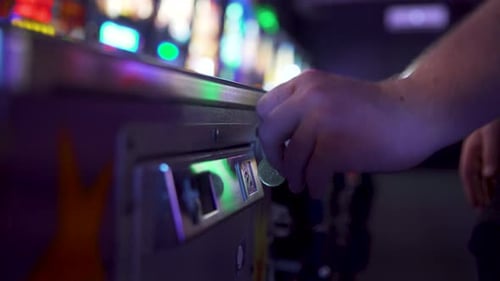 Person dropping a coin into an arcade game Pinball and pulling the spring back to shoot the ball.