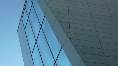 Abstract angle of a modern building with a geometric glass facade against a clear sky.