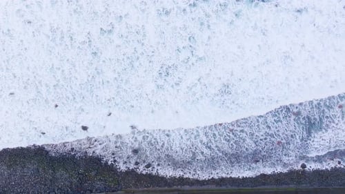 Waves crashing on rocky shore captured from above in a coastal landscape