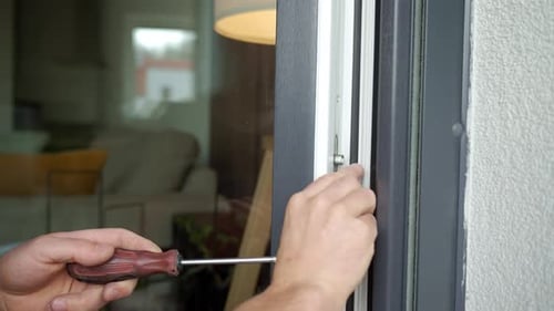 Man Repairing a White Window with a Screwdriver