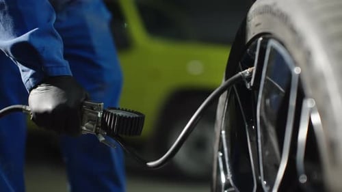 Nahaufnahme eines Mechanikers, der einen Autoreifen mit einem Manometer und einem Prüfrad für den Luftschlauch aufpumpt