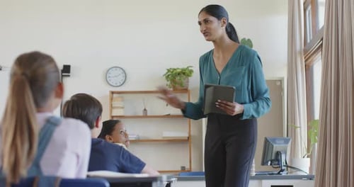 In school, teacher holding tablet and engaging with students in classroom