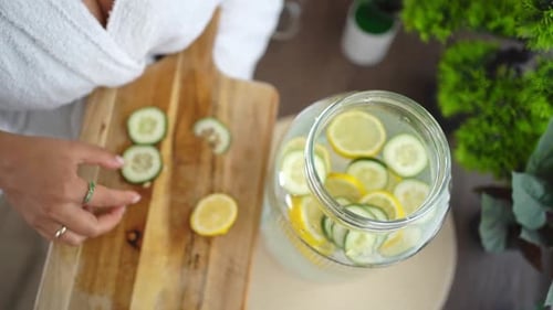 Beautician adding cucumber and lemon slices to a jar of detox water