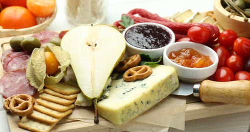 Charcuterie board with many different snacks on table, closeup. Camera moving right