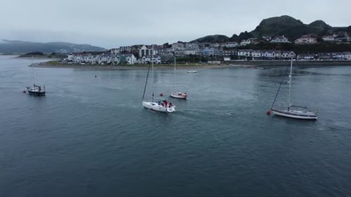 Aerial follow view behind yacht navigating seaside mountain Welsh town quiet river Conwy estuary