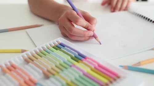 Child Drawing with Colored Pencils on White Table