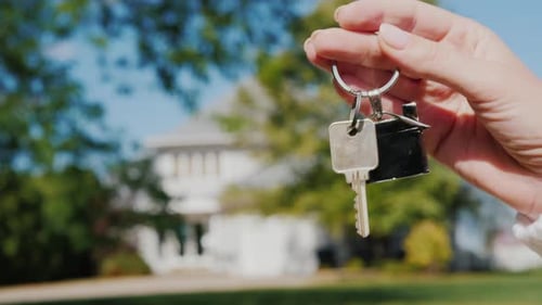 Hand Holds House Keys in Front of New Home