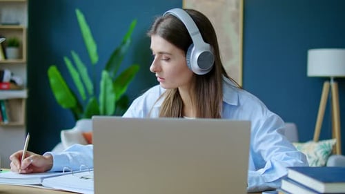Woman Writing Notes at Desk With Laptop