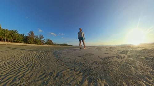 Low Angle Wide View of Man Standing Still on Beach While Camera Moves Around Him Creating Rotating P