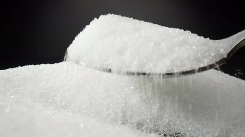 Ein Löffel, der vorsichtig schneeweiße Zuckerkörnchen schöpft