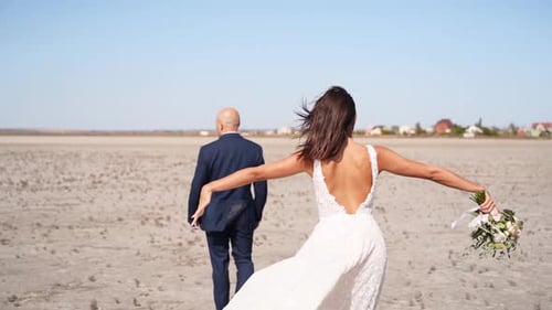 Happy Newlyweds Going at the Desert Landscape Pretty Bride with a Delicate Bouquet and Groom in Suit