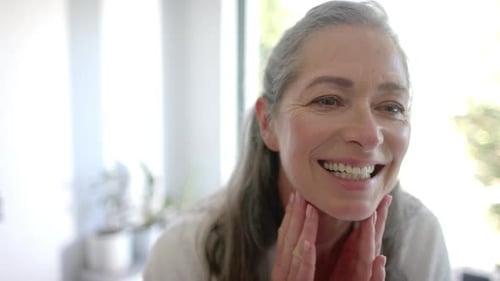 Woman Smiles and Touches Face in Bright Bathroom