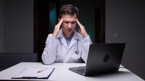 Stressed Doctor Rubbing Temples at Desk