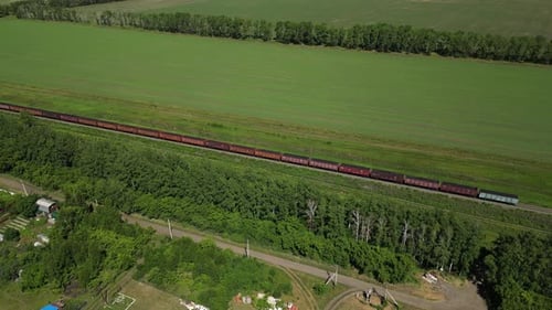 Freight Train Winding Through Verdant Countryside Passing Rural Village with Lush Green Fields and