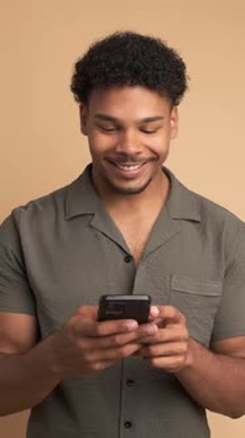 Cheerful Young Man Using Smartphone in Beige Studio