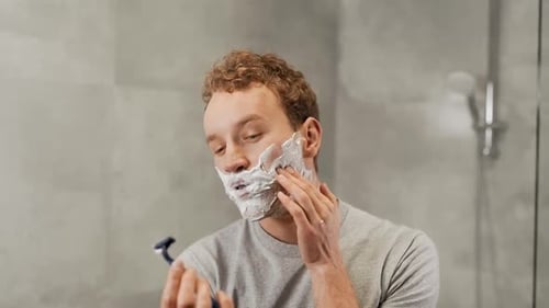 Handsome young guy shaves his beard with a razor
