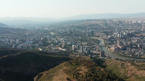 Aerial wide angle view of city of Tbilisi in Georgia disappearing behind a mountain. Establishing sh