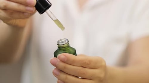 Woman Holding Dropper and Green Bottle