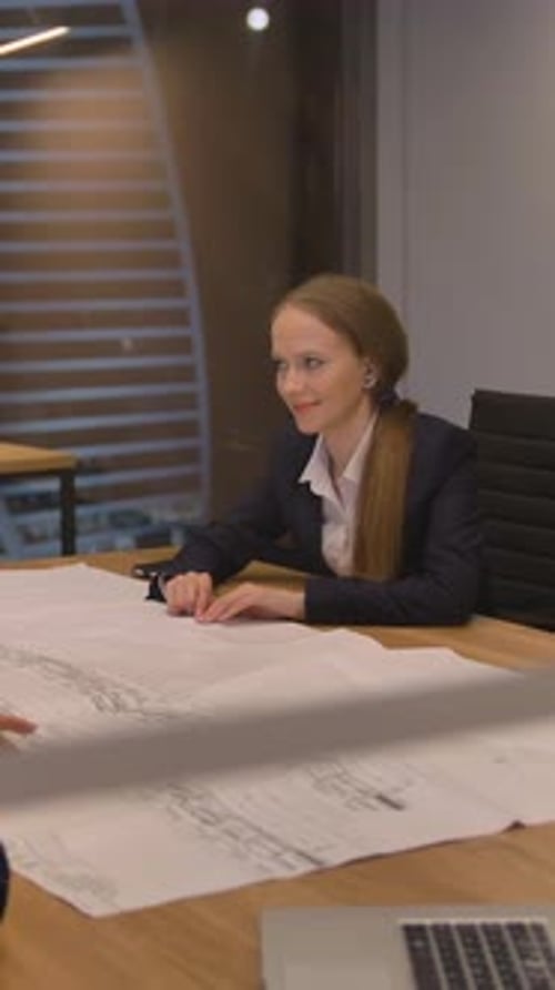Vertikal von Im modernen Büro Drei Mitarbeiter am Tisch schauen auf das Zeichenpapier und reden