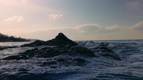Slow Motion Ocean Waves Crashing Against Dark Volcanic Rocks At Sunset, Water Spray Frozen In Air