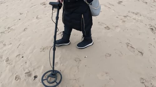 Person walking across soft beach sand while sweeping a metal detector over scattered footprints,