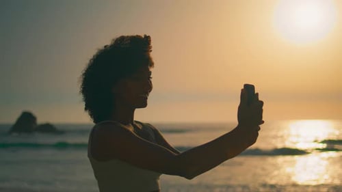 Silhouette of Woman Taking Photo at Beach Sunset