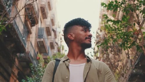 Close up, young smiling man walks along the narrow street of the old city and looks around