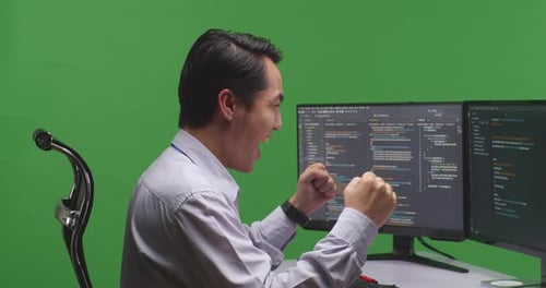 Happy Asian Developer Celebrating While Write Code With Multiple Computer Screens In Green Screen