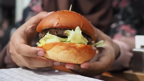 Hand Holding Beef Burger on Table Close Up