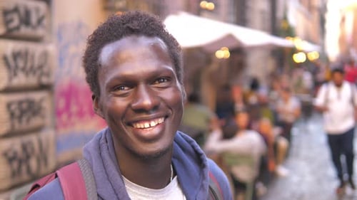 hope, confidence - young african man on the crowded street smiles at the camera