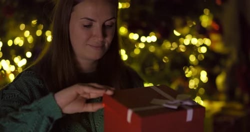 Woman Opens Christmas Gift with Joyful Expression