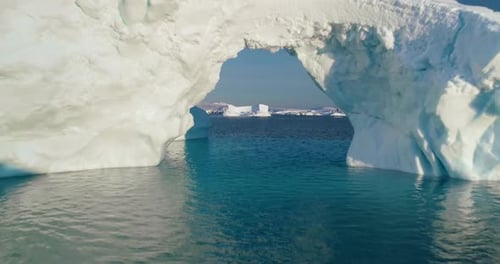 Arch in Melting Arctic Iceberg Floating Blue Ocean
