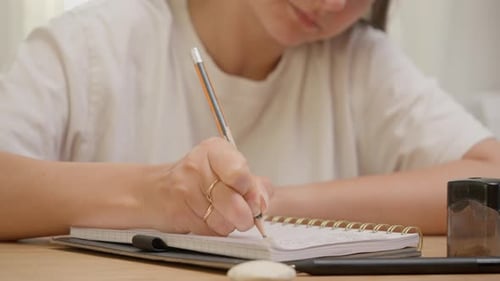 Woman writing in notebook with pencil on wooden table