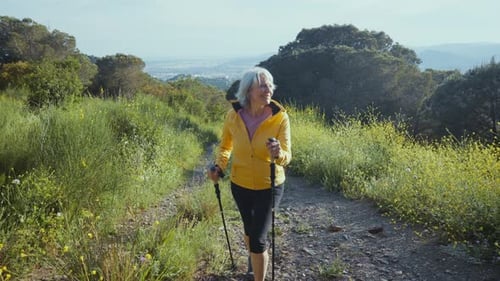 Energetic senior woman walking on mountain path with trekking poles