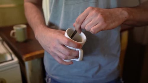 Man Stirs Beverage with Spoon in Mug