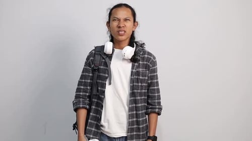 Young Asian college student sneezes into tissue. Isolated guy is sick, has a cold or allergic