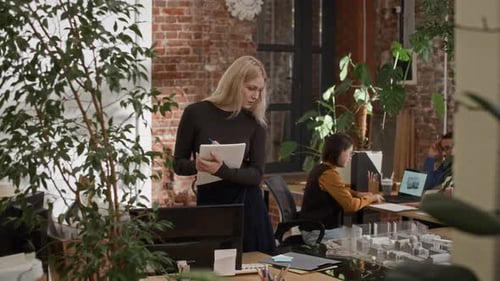 Young Female Architect Writing Notes while Reviewing 3D Layout in Modern Office