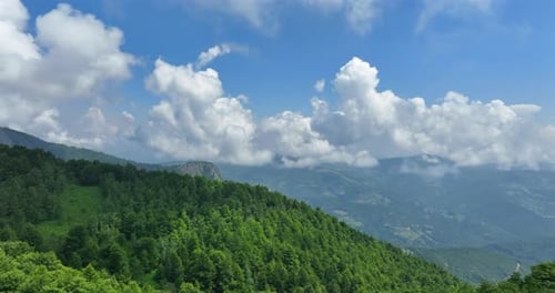 Flight over green mountain peaks. A beautiful sunny summer day at high altitude with thick clouds an