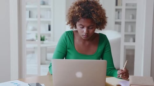 Woman Working on Laptop and Writing in Notebook