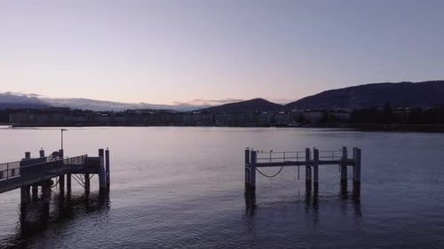 Vorwärts: Fliegen Sie über den Pier im See. Leicht gewellte Wasseroberfläche, die den Dämmerungshimmel reflektiert, Genf