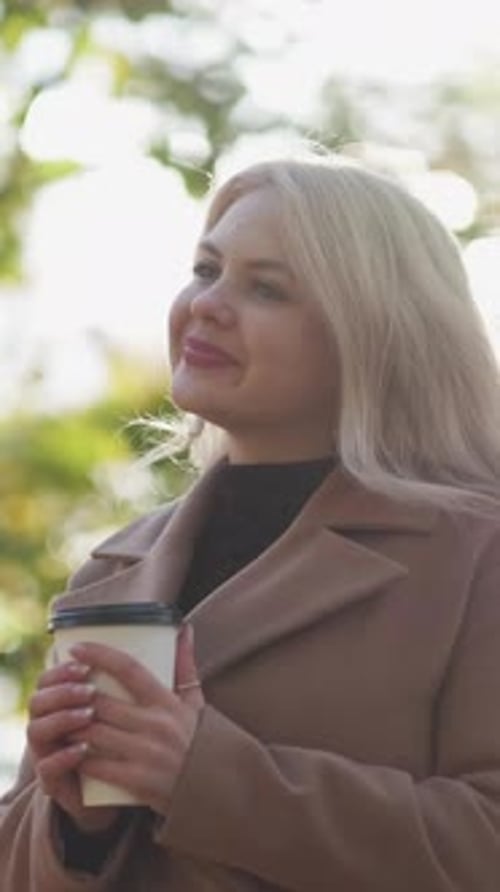 Woman Smiling and Holding Coffee Outdoors in Autumn