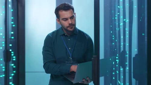 An IT Professional is Working Efficiently in a Data Center While Using Their Laptop