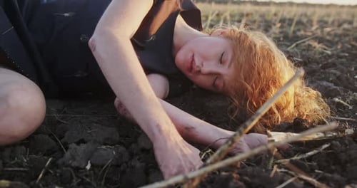 Red-Haired Woman Lying in Muddy Field at Sunset