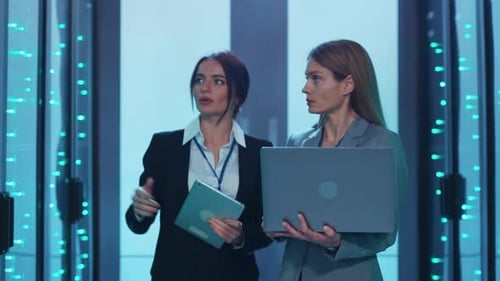 Two Women Collaborate in a Hightech Server Room Analyzing Data
