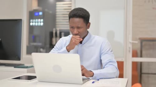 Coughing African Businessman Using Laptop in Office