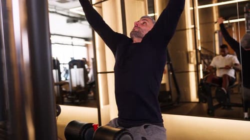 Hombre maduro que desarrolla los músculos de la espalda con una máquina Lat Pulldown