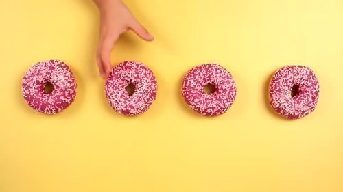 Hands Taking Frosted Donuts on Yellow Background